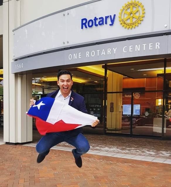 Ein junger Mann mit dunklen Haaren macht einen Luftsprung vor dem Eingang zum One Rotary Center. In seinen Händen hält er die Flagge von Chile.